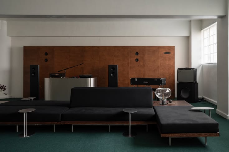 Lounge with a low black sofa, a wood-paneled wall with speakers and a turntable, and green carpet